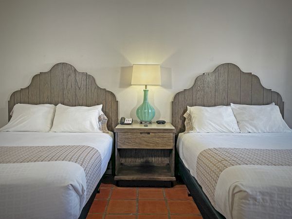 The image shows a hotel room with two beds, a nightstand in between, and a lamp atop it.