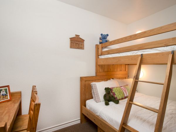 A cozy bedroom with wooden bunk beds, teddy bears, a desk with a framed photo, and a wooden wall decoration.