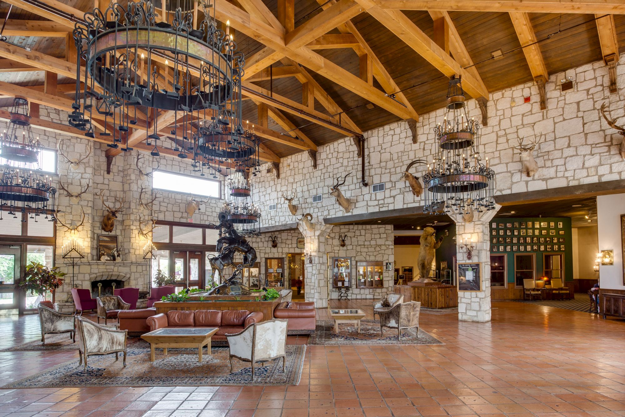The image shows a spacious, rustic hotel lobby with wooden beams, stone walls, large chandeliers, and comfortable seating.