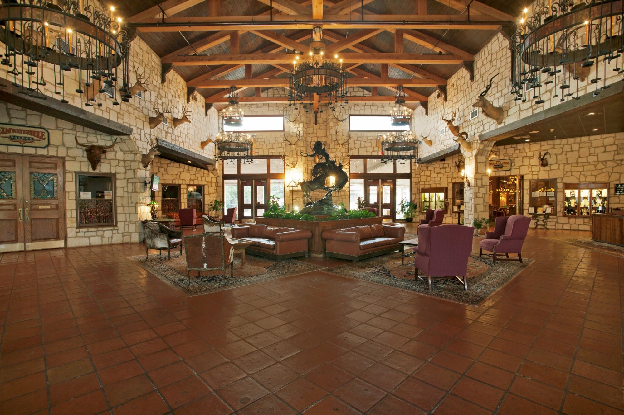 A spacious lobby with rustic decor, wooden beams, plush chairs, and a central sculpture, creating an inviting and cozy atmosphere.
