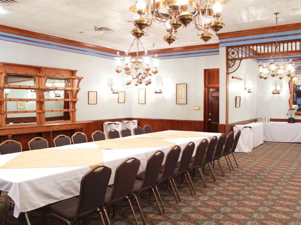 A banquet room with a long table, chairs, chandeliers, and sideboard in a classic setting.