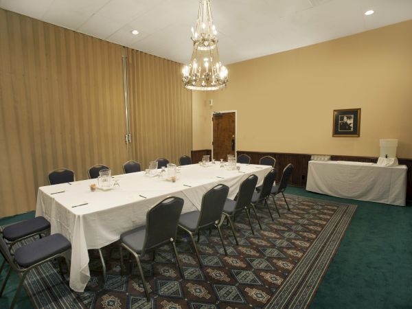 The image shows a conference room with a long table, chairs, a chandelier, and a cabinet against the wall, set for a meeting.