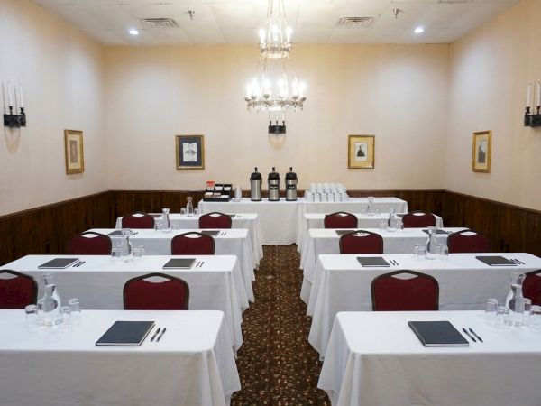 A formal banquet room with set dining tables, place settings, and chandeliers lighting the space for an event.