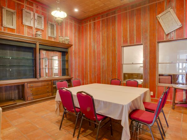The image shows a dining room with red walls, a table covered with a white cloth, and red chairs around it.