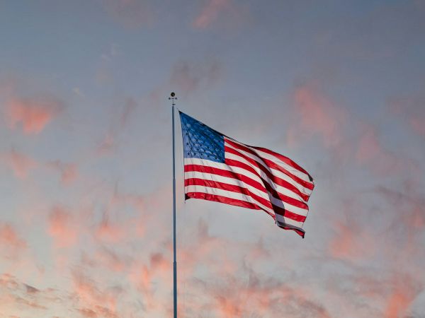 An American flag waves against a backdrop of a cloudy, pink-hued sky.