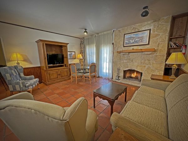A cozy living room with a fireplace, armchairs, a sofa, TV, wooden furniture, and warm lighting creating a relaxing atmosphere.