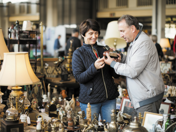 A man and woman are looking at an item in an antique store, surrounded by lamps and collectibles, while smiling.