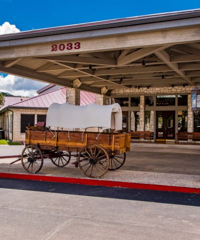 A vintage wooden wagon sits under a stone-fronted entrance with the address 2083, parked on a curb in front of a building.