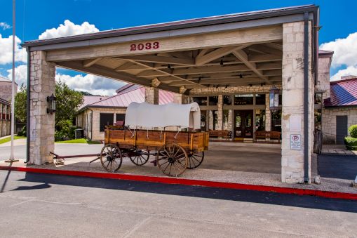 A vintage wooden wagon sits under a stone-fronted entrance with the address 2083, parked on a curb in front of a building.