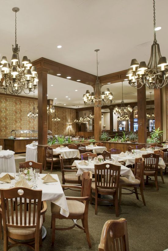 The image shows an elegant restaurant with round tables, chandeliers, and wooden decor, providing a spacious dining atmosphere.