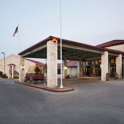 The image shows a building with a covered entrance, a U.S. flag, stone walls, and a horse-drawn carriage displayed outside.
