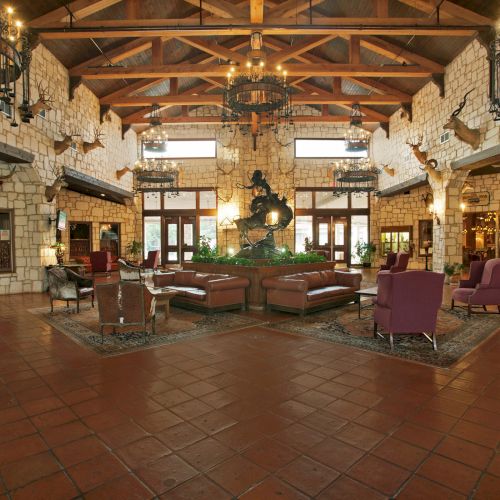 The image shows a spacious lobby with a high wooden ceiling, seating areas, chandeliers, and decorative elements on the walls.