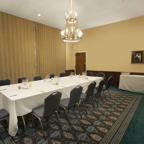 The image shows a conference room with a long table covered in white cloth, surrounded by chairs, and a chandelier hanging above.
