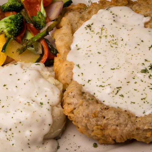 The image shows a plate with chicken-fried steak topped with gravy, mashed potatoes with gravy, and a side of mixed vegetables.