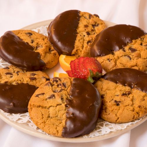 A plate with chocolate-dipped cookies arranged in a circle, garnished with a strawberry and a slice of orange is displayed.