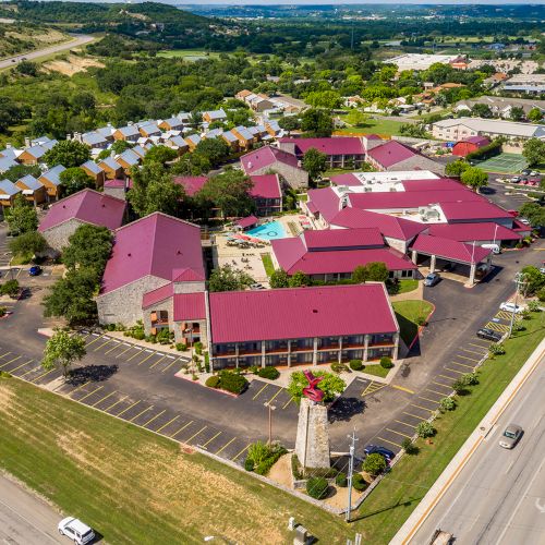 Aerial view of a large complex with red roofs, surrounded by trees and parking areas, located near roads and a semi-rural landscape.