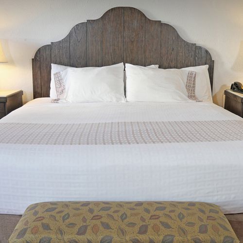 A neatly made bed with a wooden headboard, flanked by two bedside tables with lamps, and an upholstered bench at the foot.