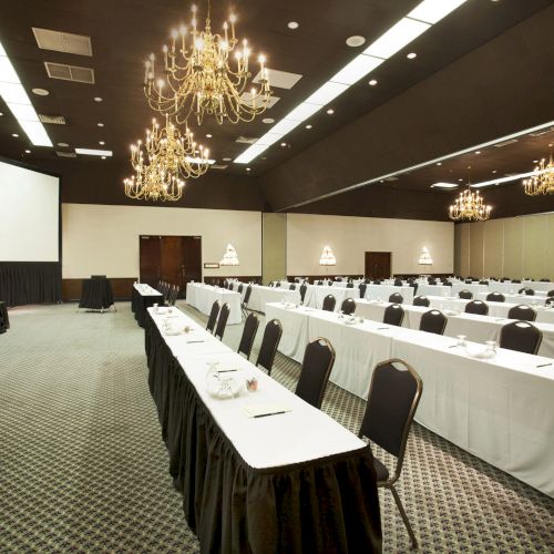 A conference room with rows of tables and chairs, chandeliers, a podium, and a projection screen.