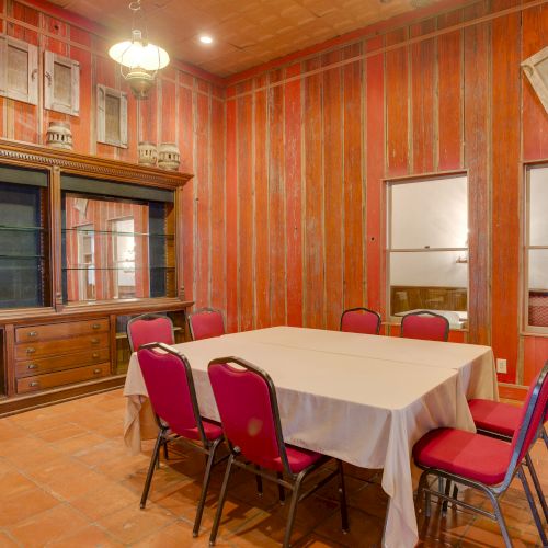 A room with red chairs around a table, wooden walls, decorative shelving, and framed items on the wall and ceiling.