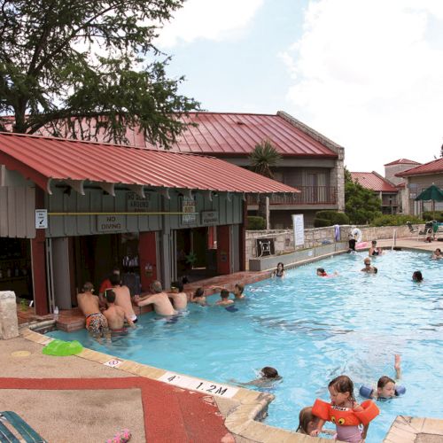 A swimming pool with people enjoying the water; there's a poolside bar and seating area under a red-roofed structure.