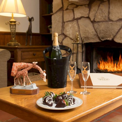A cozy living room with a stone fireplace, champagne, chocolate treats, and a giraffe figurine on a wooden table.