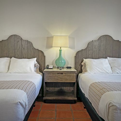 Two beds with ornate headboards, a nightstand between them, topped with a lamp and phone, create a cozy and inviting room.