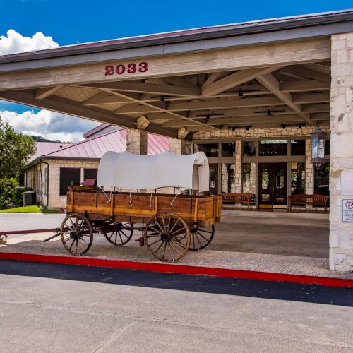An old covered wagon is displayed under a large entrance canopy with a building in the background, marked with the number 2033.