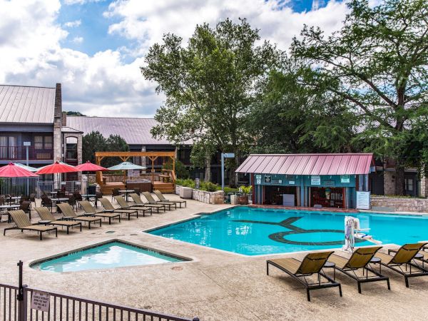 Outdoor pool area at a resort with lounge chairs, umbrellas, and a building in the background under a partly cloudy sky. End.