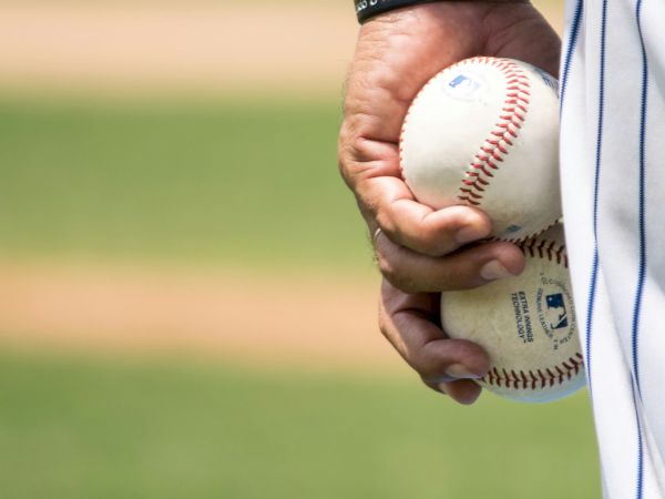 A close-up of a person gripping a baseball against a blurred field, fingers wrapped around the ball and wearing a striped uniform.
