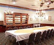 Bright dining room with white-clothed tables, dark chairs, ornate chandeliers, and a wooden bar or serving counter.