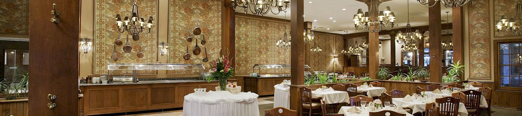 An elegant banquet hall with set tables, ornate chandeliers, and patterned wallpaper under tall ceilings.