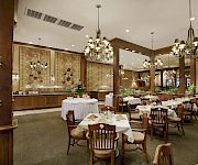 An elegant banquet hall with set tables, ornate chandeliers, and patterned wallpaper under tall ceilings.