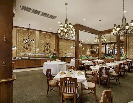 An elegant banquet hall with set tables, ornate chandeliers, and patterned wallpaper under tall ceilings.