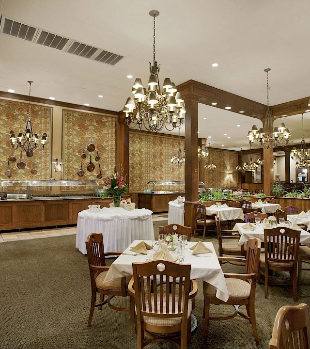 An elegant banquet hall with set tables, ornate chandeliers, and patterned wallpaper under tall ceilings.